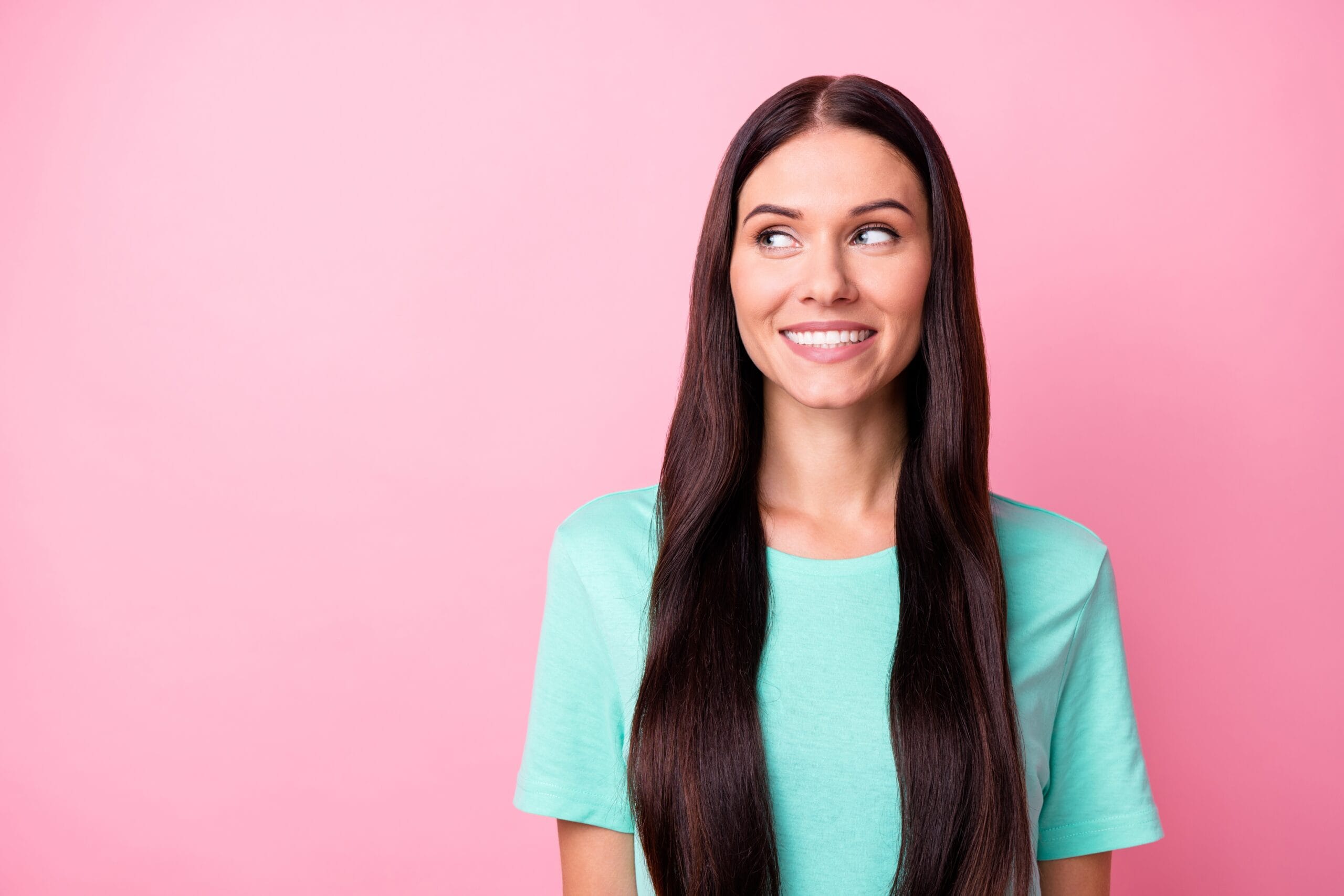 uśmiechnięta kobieta na różowym tle ze wzrokiem skierowanym w lewą stronę