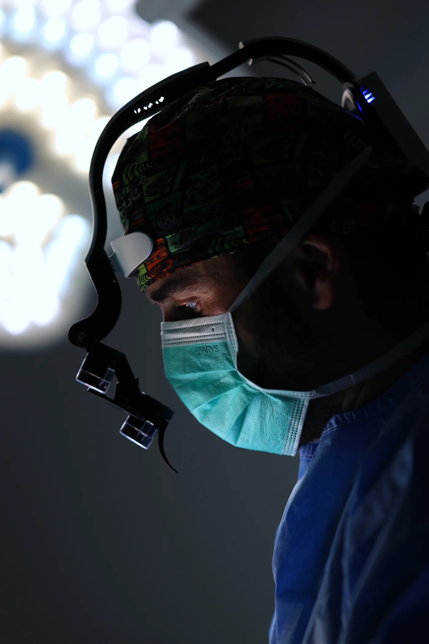 Dr n. med. Kamil Marczewski podczas zabiegu na sali operacyjnej, w masce chirurgicznej i lupach zabiegowych
